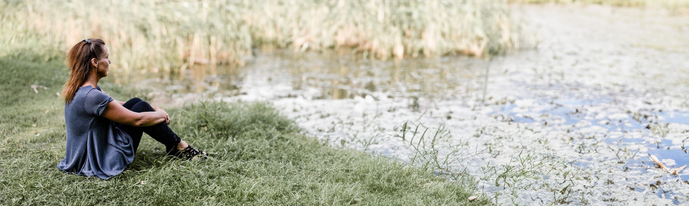 Friederike Gerling, Ausbilderin am IHvV, sitzt entspannt im Gras am Wasser