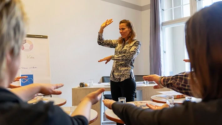 Friederike Gerling leitet eine Übung an, die Teilnehmenden machen die Handbewegung mit